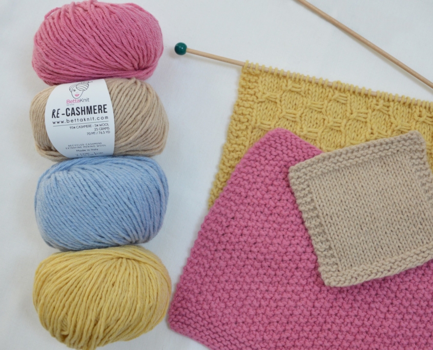 Gomitoli di cashmere rigenerato Re-Cashmere Bettaknit in diversi colori con campioni lavorati a maglia e ferri su sfondo bianco.