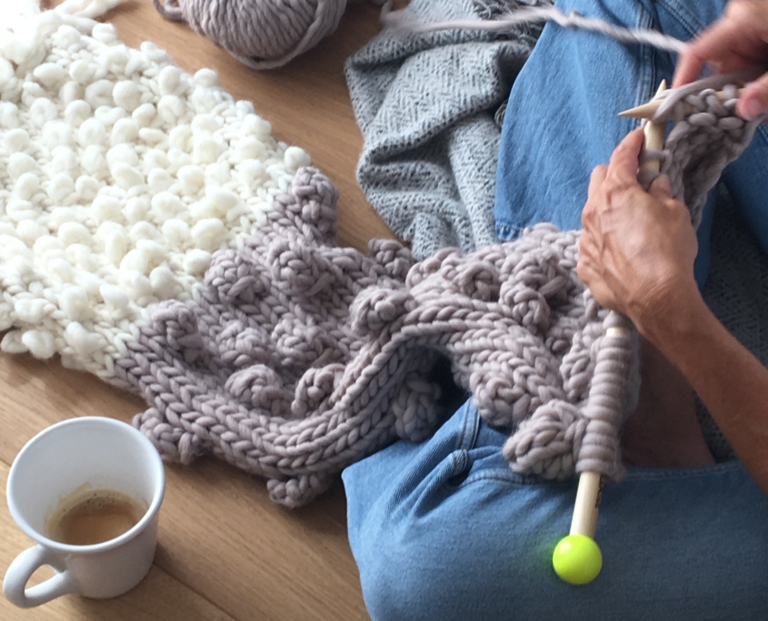 Persona che lavora a maglia con una tazza di caffè durante un momento di relax e benessere domestico.