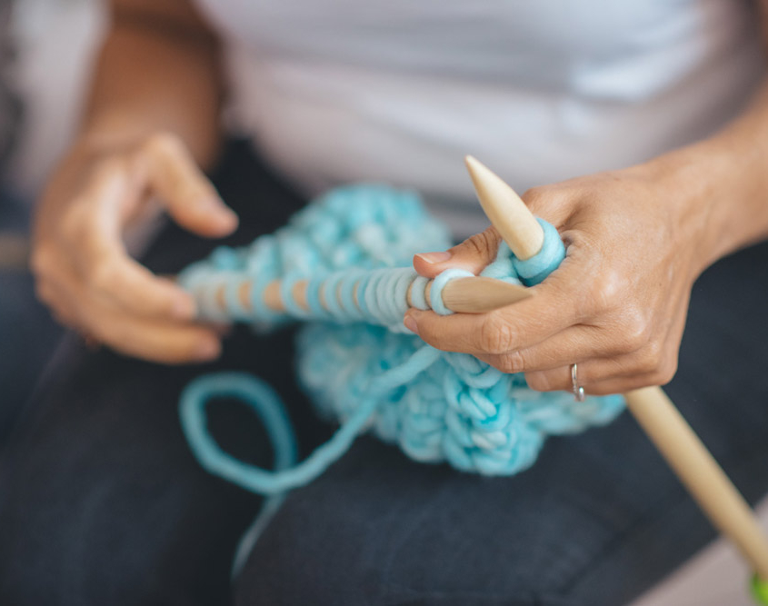 Mani che lavorano a maglia con ferri e filato azzurro durante un momento di relax e creatività.
